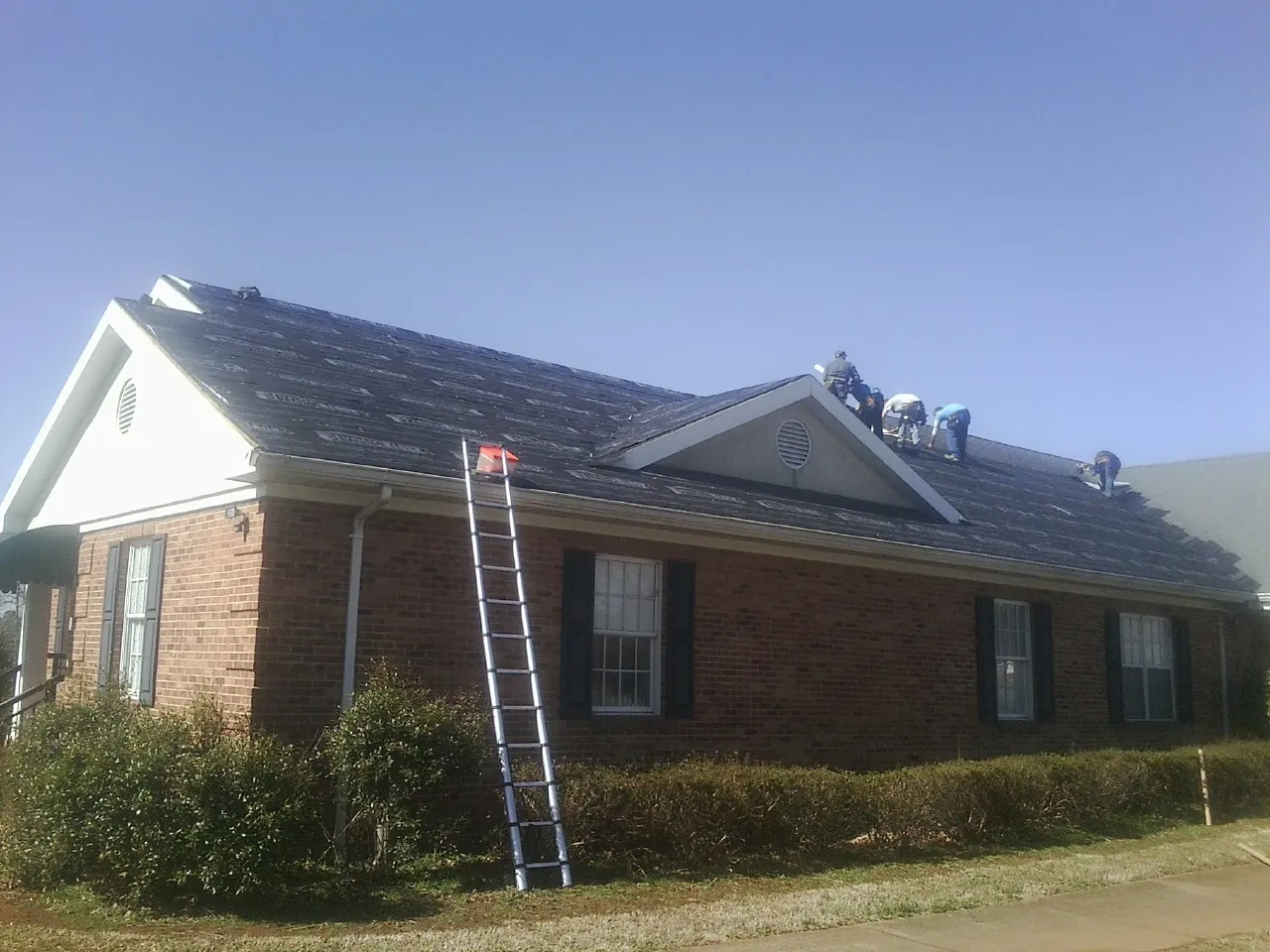 Crew tearing shingles off a brick ranch roof with a ladder set — Emergency Roof Repair work by our crew in Walhalla