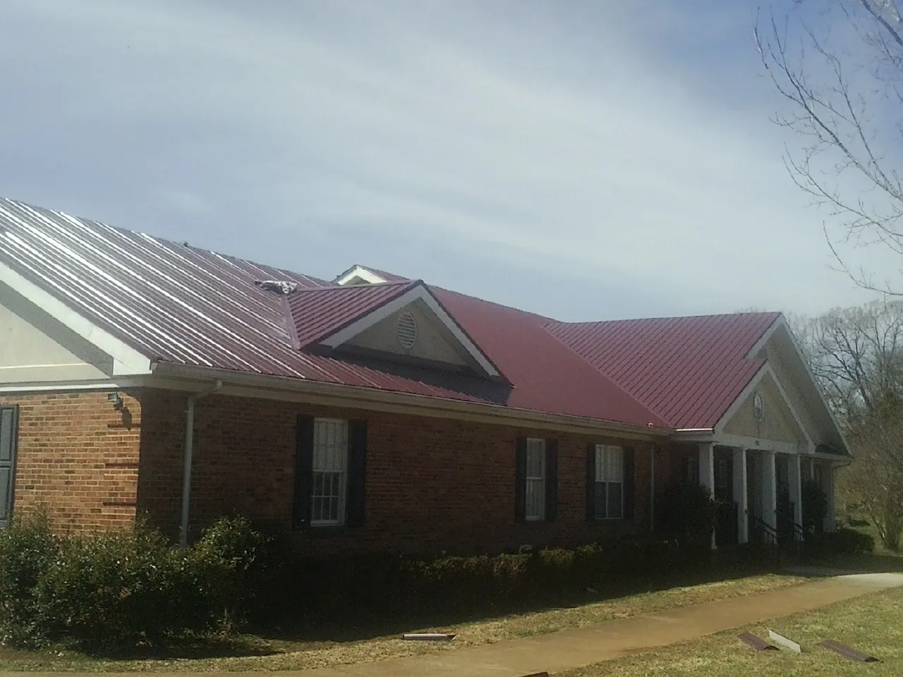 Red metal roof with gabled entries on a long brick building, from a Hail Damage Roof Repair job in Walhalla