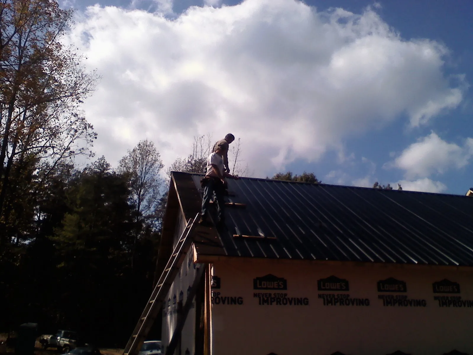 Roofer fastening dark metal panels high against a cloudy sky, from a Roof Inspection job in Walhalla
